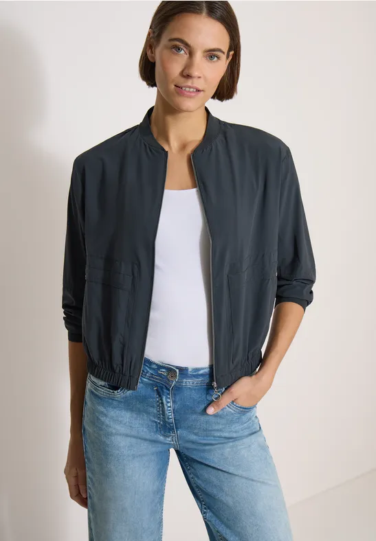 Femme porte une veste bomber bleu marine, un top blanc et un jean bleu.