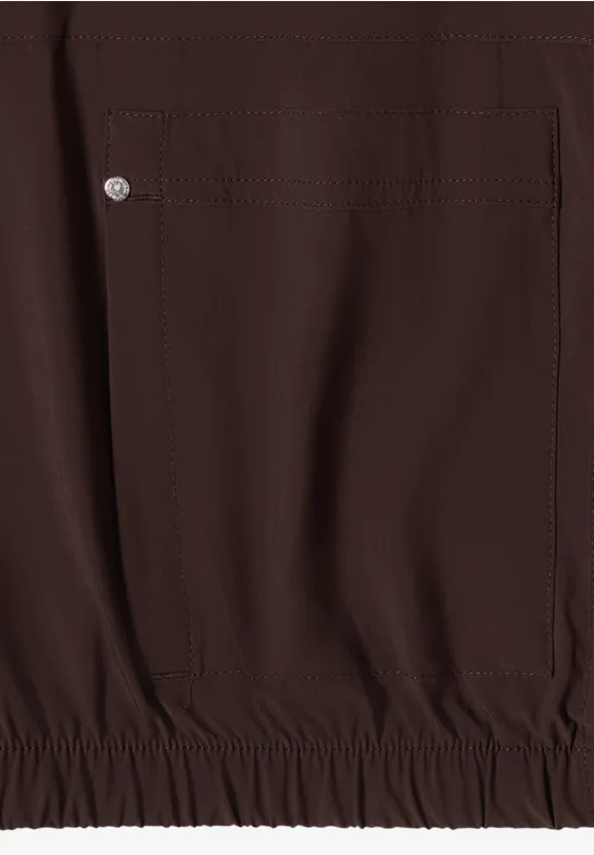 Tissu lisse marron foncé, poche latérale pressionnée et ourlet élastique d'un vêtement.