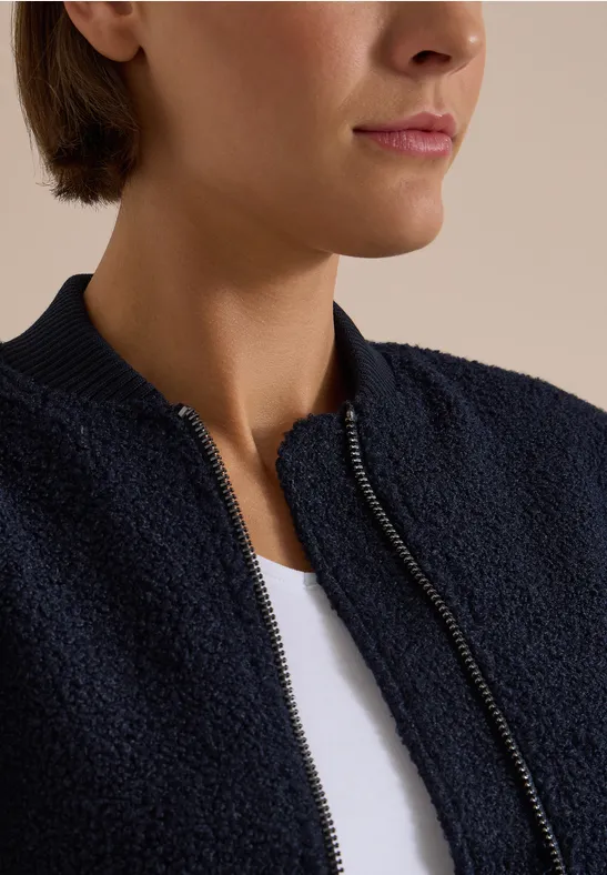Close-up van persoon met wit T-shirt en donkerblauwe, gestructureerde jas met ritssluiting.
