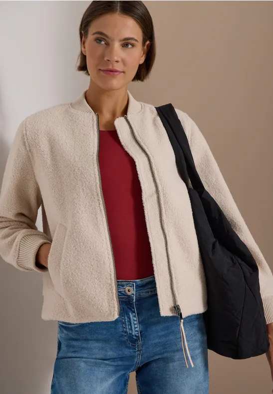 Frau in beiger Jacke, rotem Top, Jeans und schwarzer Tasche.