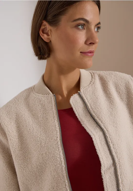 Eine Frau in beiger Teddy-Fleecejacke und rotem Top blickt seitlich.