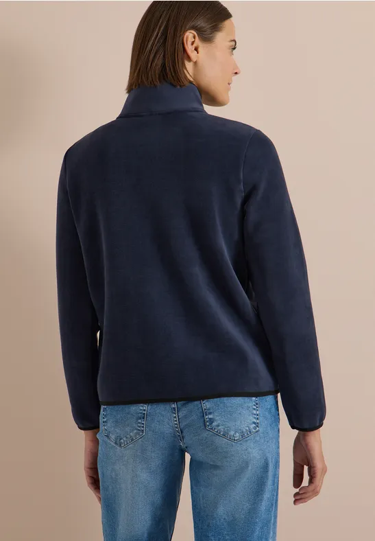 Frau steht mit dem Rücken zur Kamera und trägt einen dunkelblauen Fleece-Pullover und blaue Jeans.