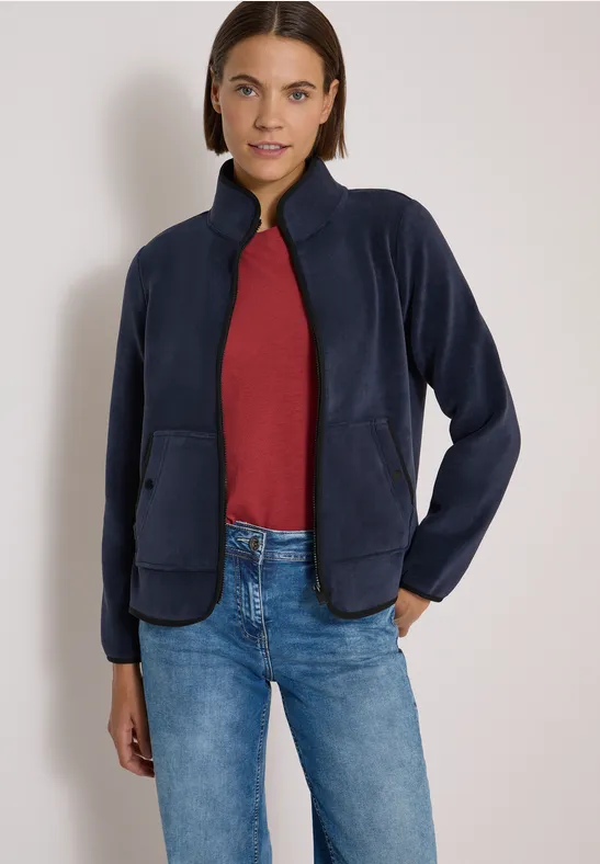 Junge Frau trägt dunkelblaue Fleecejacke, rotes Shirt und Jeans.