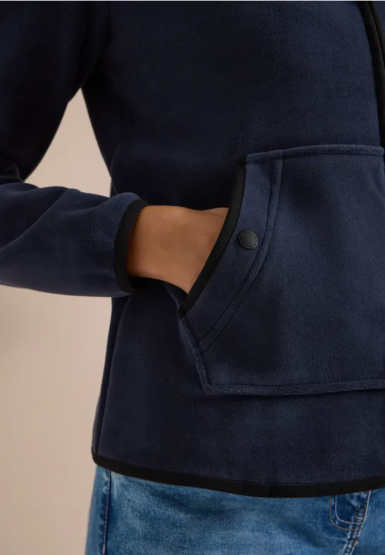 Person trägt dunkelblaue Fleecejacke mit Kängurutasche, Hand in Tasche, kombiniert mit Jeans.