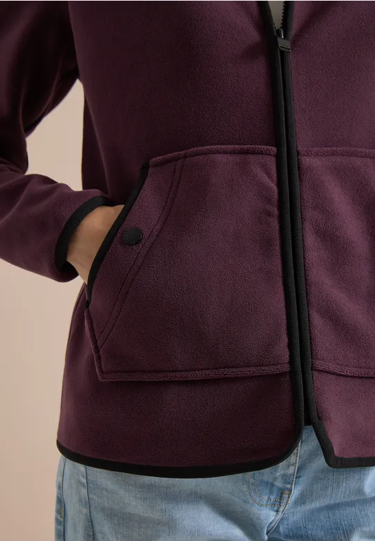 Iemand draagt een pruimkleurig jasje met zwarte bies, twee zakken en een lichtblauwe jeans.