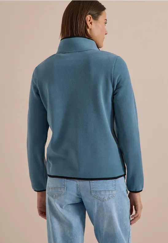 Rückansicht einer Frau in türkiser Jacke und Jeans.