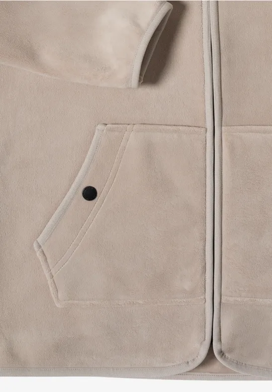 Nahaufnahme einer beigen Fleecejacke mit aufgesetzter Tasche und schwarzem Druckknopf.