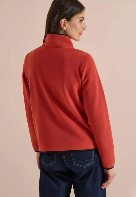Vrouw met rood fleecejack van achter, draagt blauwe jeans, kijkt zijwaarts naar links