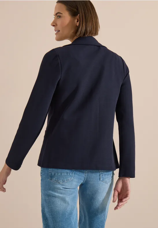Vue de dos d'une personne portant une veste bleu foncé et un jean bleu clair sur fond beige.