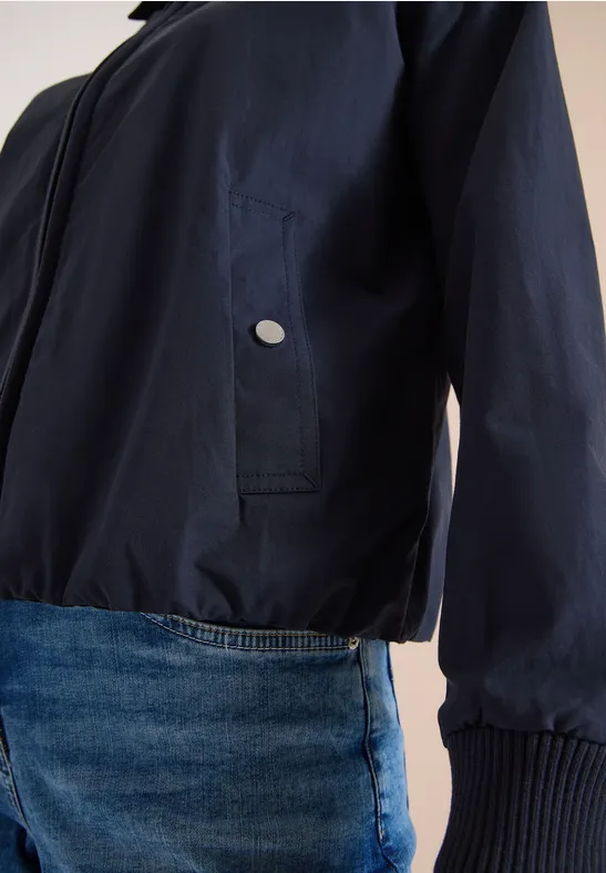 Dunkelblaue leichte Jacke mit seitlicher Tasche und blauer Jeans im Hintergrund