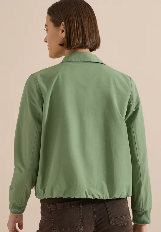 Personne aux cheveux courts porte une veste verte et un pantalon marron, vue de dos.