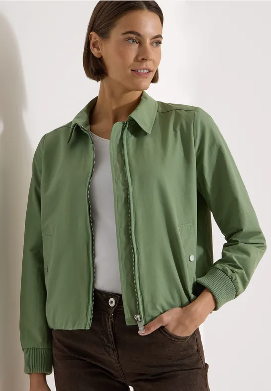 Personne porte une surchemise verte, un débardeur blanc et un pantalon marron dans un style épuré.