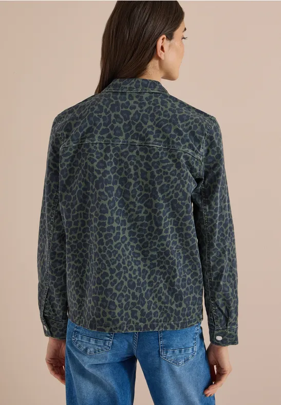 Frau von hinten in blau-grün gemusterter Jeansjacke vor beigem Hintergrund.