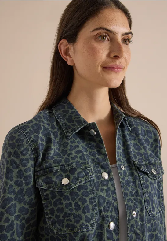 Frau mit langem braunen Haar trägt grüne Jeansjacke mit Leopardenmuster.