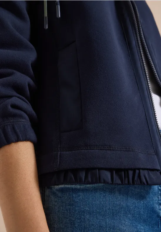 Close-up van een persoon in een donkerblauw jack en blauwe spijkerbroek.