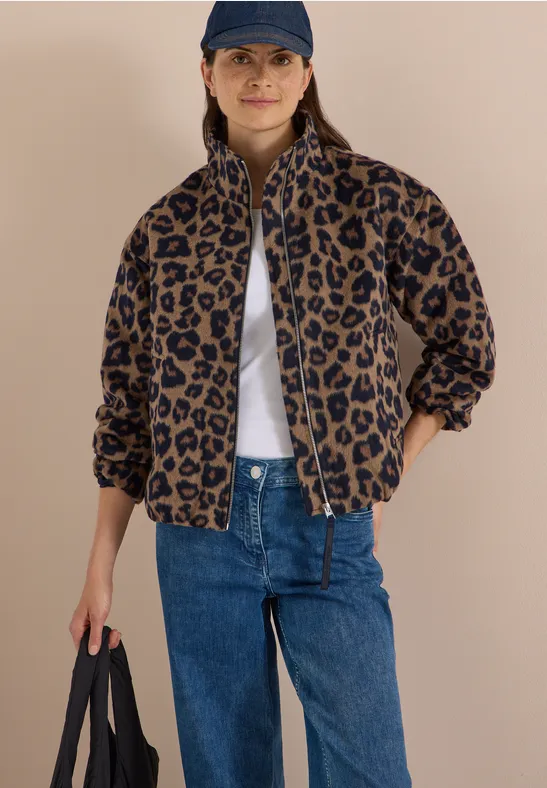 Vrouw in luipaardfleecejack, blauwe jeans, pet en wit shirt, met zwarte tas, nonchalante en stijlvolle uitstraling.