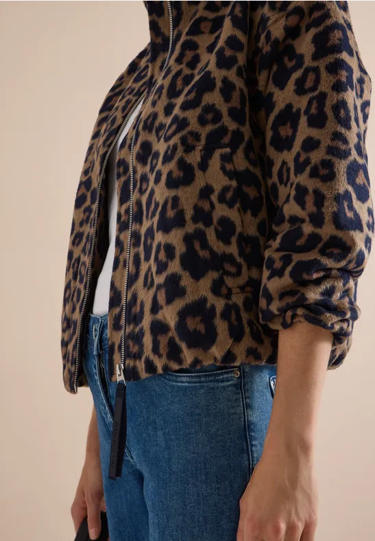Gedeeltelijke weergave van een persoon in blauwe jeans en een luipaardprint jack met rits.