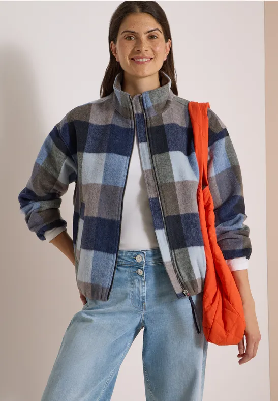 Femme en veste à carreaux bleu-gris, t-shirt blanc, jean clair et sac rouge porté sur l'épaule