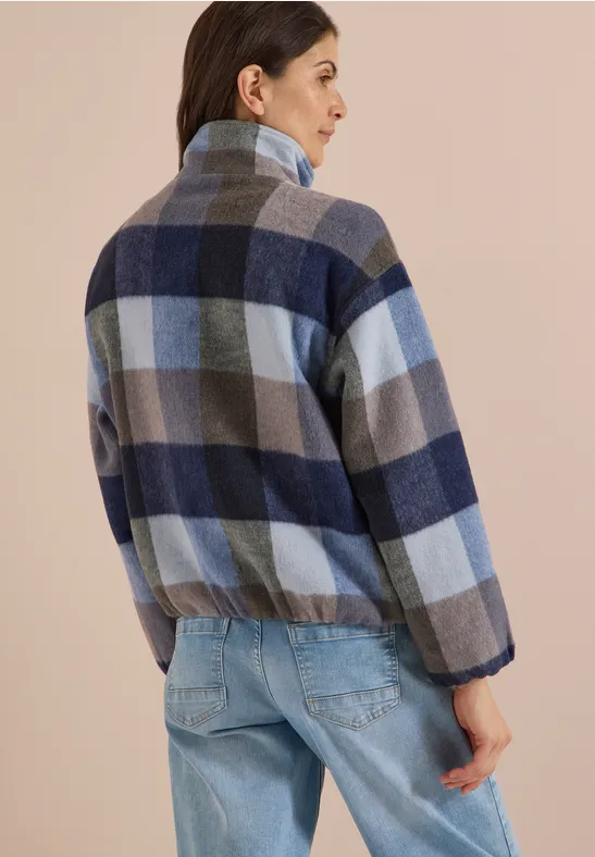 Un homme de dos porte une veste en polaire à carreaux, col montant et bords élastiques, avec un jean.