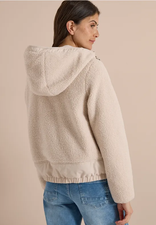 Frau in hellbeiger, kuscheliger Teddy-Fleece-Jacke mit Kapuze, Rückansicht.