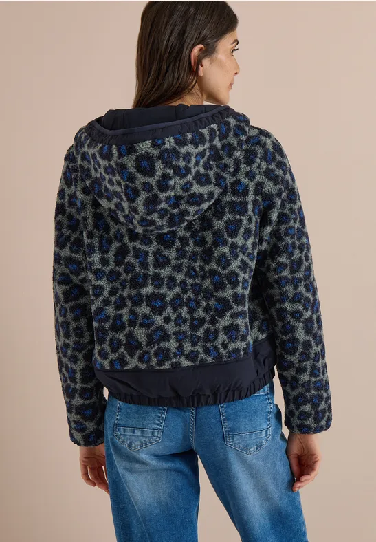 Een vrouw van achteren in een blauwe luipaardjas met capuchon en spijkerbroek.