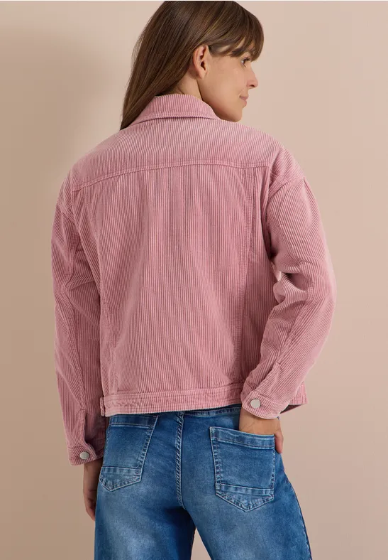 Une femme vue de dos portant une veste rose en velours côtelé et un jean bleu.