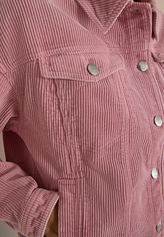 Gros plan d'une veste en velours côtelé rose à boutons-pression argentés et poche latérale.