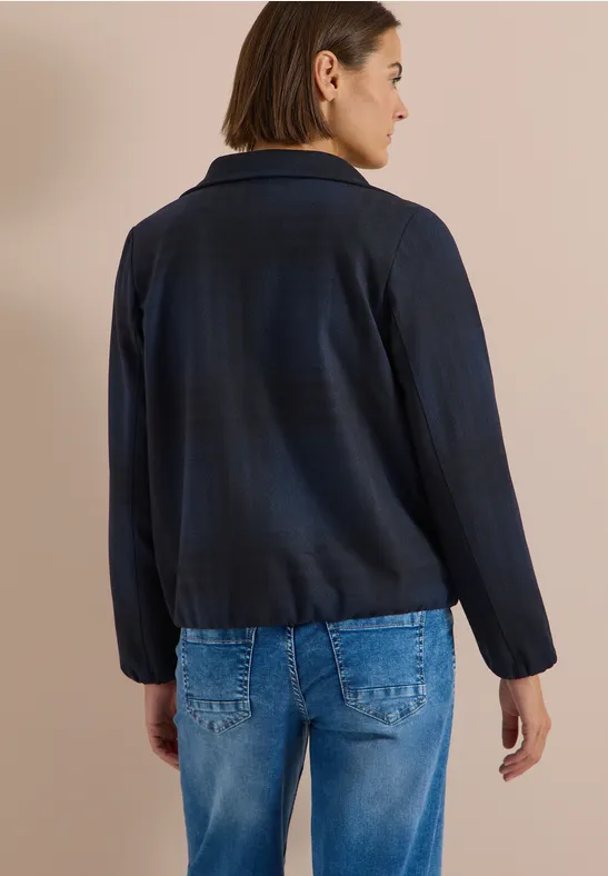 Frau von hinten in dunkelblauer Jacke mit Schalkragen und blauen Jeans