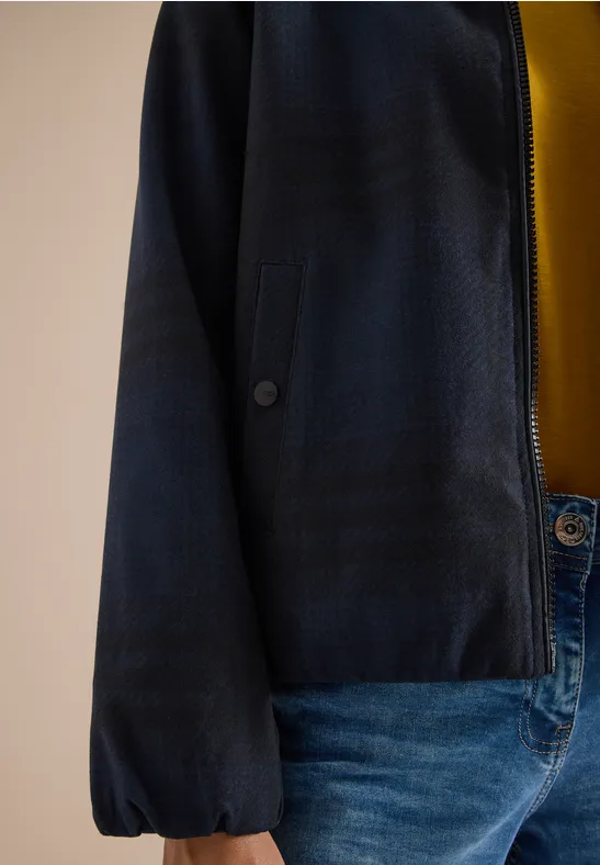 Eine Person trägt eine dunkelblaue Jacke mit Bündchenärmeln, ein gelbes Shirt und blaue Jeans.