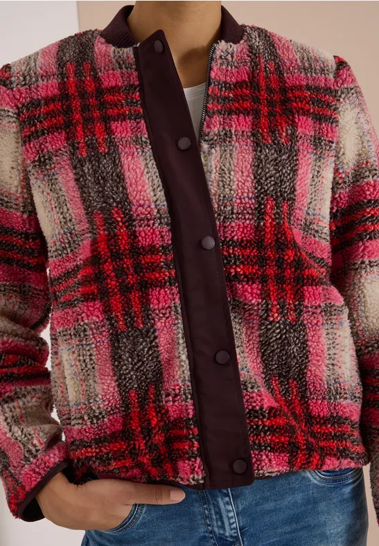 Frau trägt karierte rosa-rote Bouclé-Jacke mit lila Knopfleiste und blauen Jeans.