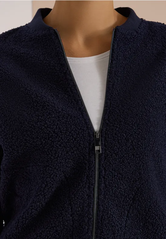 Dunkelblaue Teddy-Fleecejacke mit Reißverschluss über weißem Shirt.