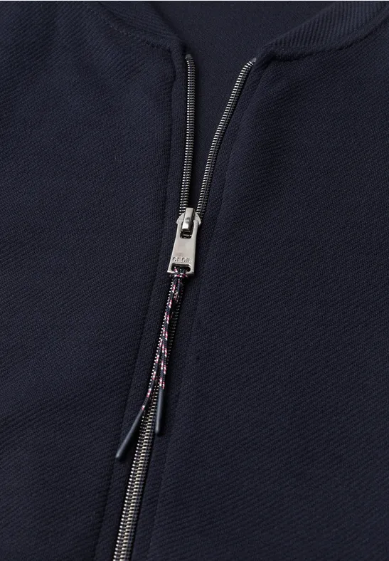 Close-up van een donkerblauwe, gestructureerde jas met een zilverkleurige rits en gevlochten koord
