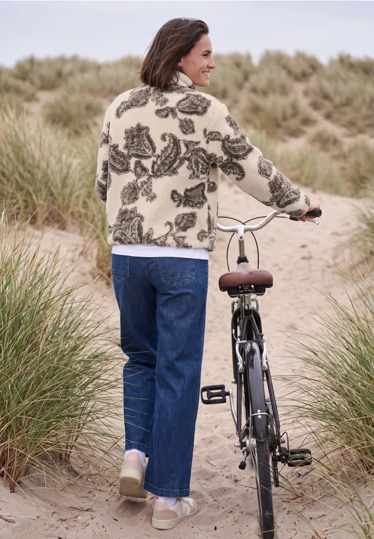 Eine Frau schiebt ihr Fahrrad auf einem Dünenweg, umgeben von Strandgras.