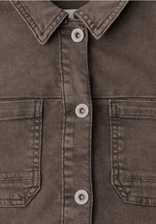 Nahaufnahme einer braunen Jeansjacke mit Kragen, Knopfleiste und zwei aufgesetzten Brusttaschen.