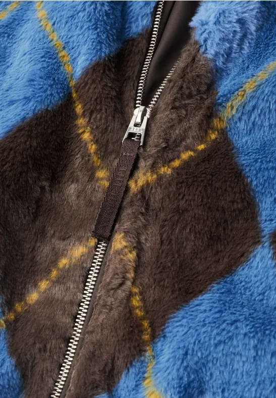 Nahaufnahme einer flauschigen Jacke mit blau-braunem Rautenmuster und Reißverschluss