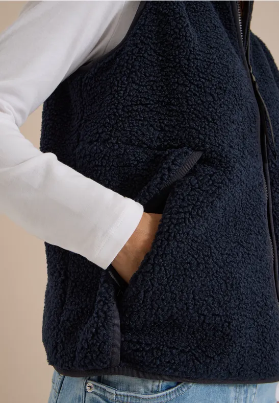 Dunkelblaue Teddy-Fleece-Weste mit Reißverschluss über weißem Langarmshirt, Hand in Tasche.