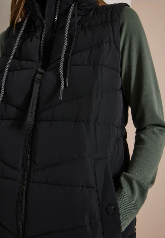Veste matelassée noire à capuche portée sur un t-shirt vert foncé à manches longues.