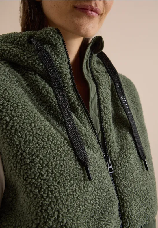 Gros plan d'une personne portant un sweat à capuche teddy vert olive avec zip et cordons noirs.
