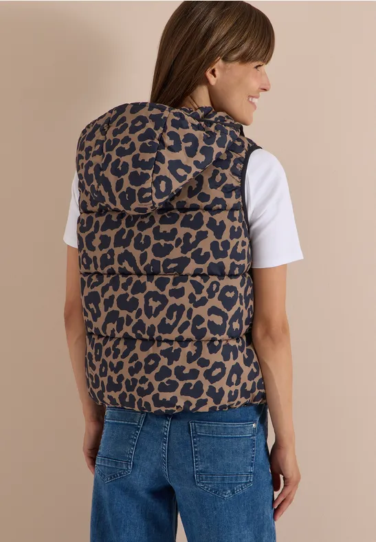 Frau von hinten in Jeans und weißem T-Shirt trägt eine ärmellose Steppweste mit Leopardenmuster und Kapuze.