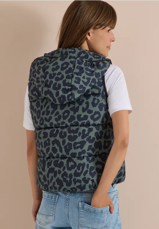 Frau von hinten im weißen T-Shirt und ärmelloser Kapuzenweste mit Leopardenmuster, Hand in Jeans-Tasche.