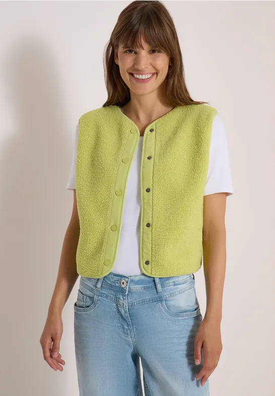 Eine Frau trägt eine grüne Knopfweste über weißem T-Shirt und Jeans.