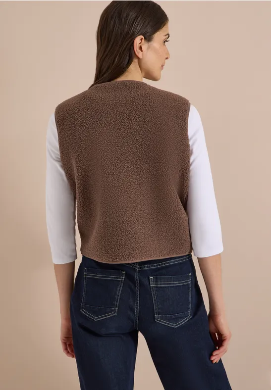 Frau von hinten in brauner Teddy-Weste über weißem T-Shirt und blauen Jeans.