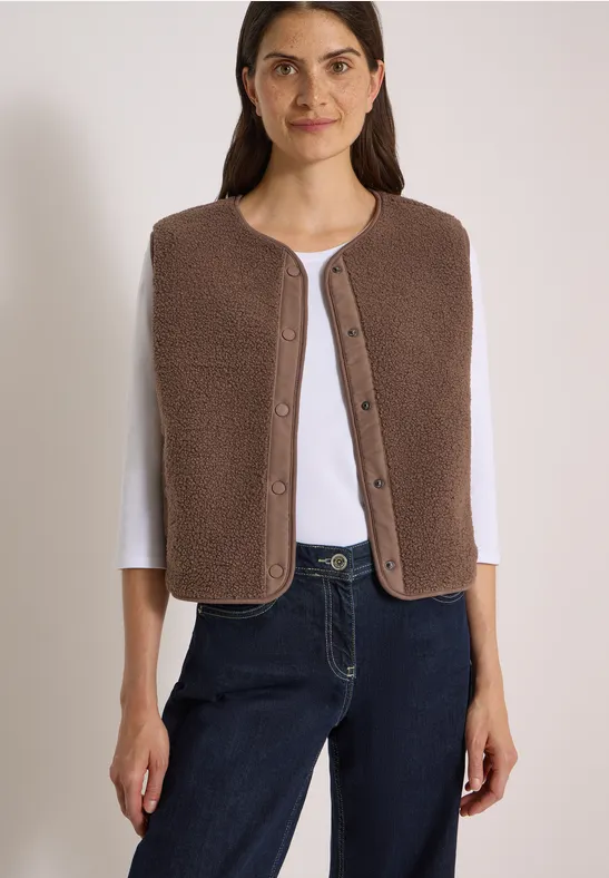Frau trägt braune Wollweste über weißem Shirt und Jeans.