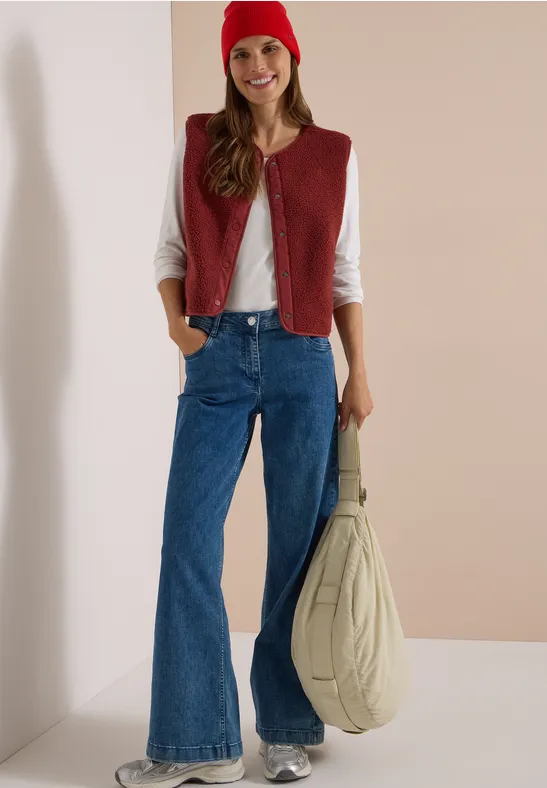 Frau mit roter Mütze, roter Weste, weißem Shirt, weitem Jeans und großer Tasche.