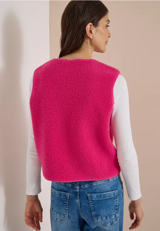 Eine Frau von hinten in einem pinken, flauschigen Strickweste, weißem Langarmshirt und blauen Jeans.