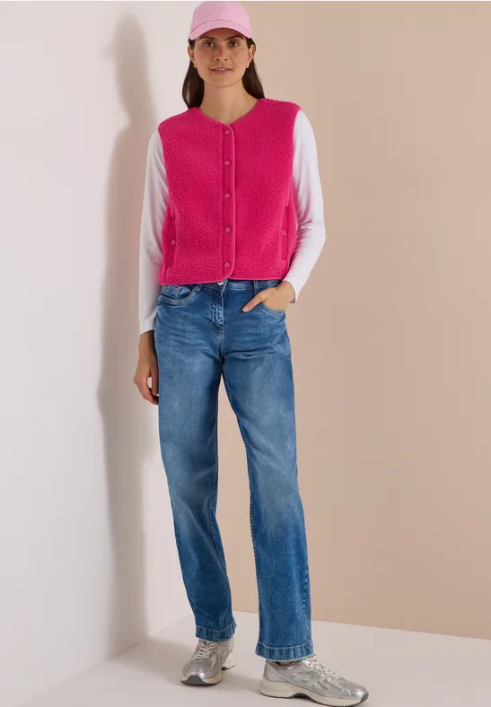 Frau trägt pink-weiße Strickjacke, blaue Jeans, graue Sneaker und pinke Baseballcap