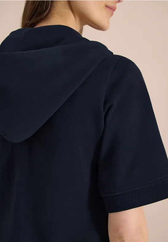 Eine Person von hinten in einem dunkelblauen kurzärmeligen Kapuzenshirt