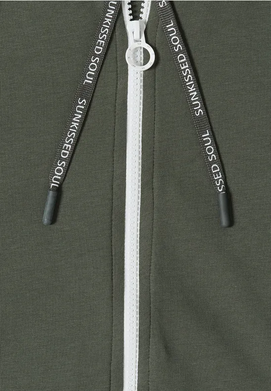 Grünes Kleidungsstück mit weißem Reißverschluss und schwarzen Kordeln mit weißem Aufdruck.