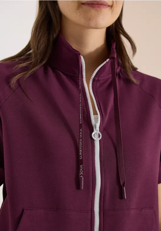 Bordeauxfarbene Damenjacke mit kurzem Arm, hohem Stehkragen, weißem Reißverschluss und schwarzen Kapuzenkordeln.