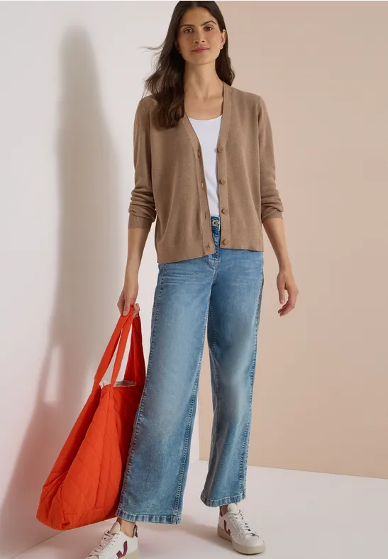 Eine Frau trägt Cardigan, weißes Top, weite Jeans, weiße Sneaker und hält eine große rote Tasche.
